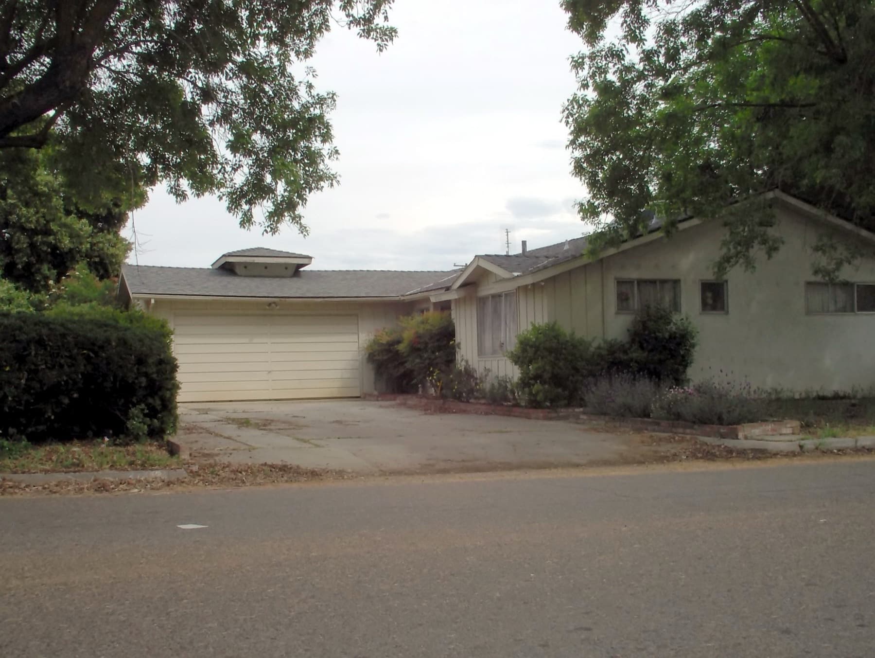 Ordinary mid-century ranch home with attached garage and mature trees — the kind of everyday house we buy as-is